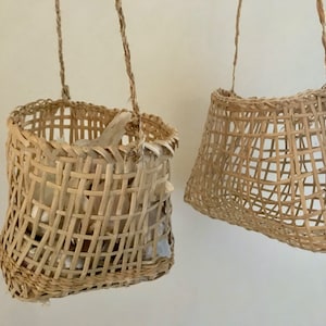 May include: Two woven baskets hanging from the ceiling. The basket on the left is filled with white garlic cloves. Both baskets are made of natural materials and have a light brown color.