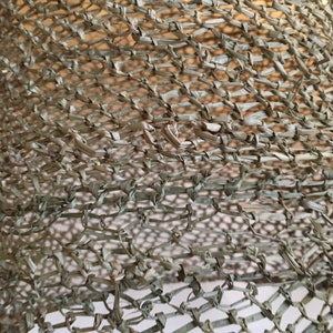 May include: Close-up of a woven, light brown, mesh material. The material is made of thin, braided strands that are woven together to create a grid pattern.