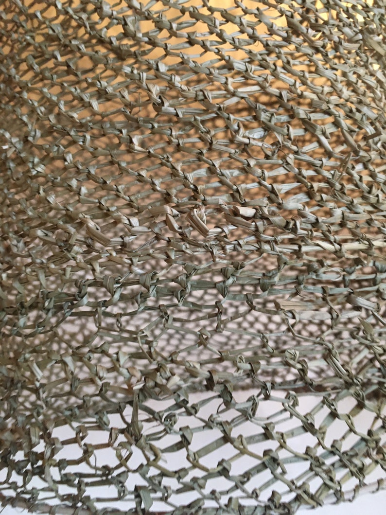 May include: Close-up of a woven, light brown, mesh material. The material is made of thin, braided strands that are woven together to create a grid pattern.