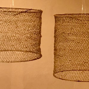 May include: Two woven lampshades made of natural fibers, hanging from the ceiling. The lampshades are cylindrical and have a light brown color.