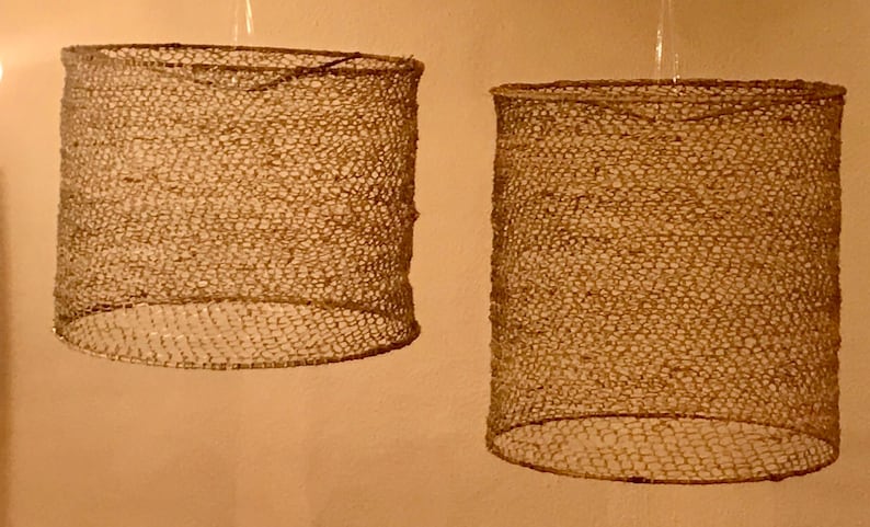 May include: Two woven lampshades made of natural fibers, hanging from the ceiling. The lampshades are cylindrical and have a light brown color.