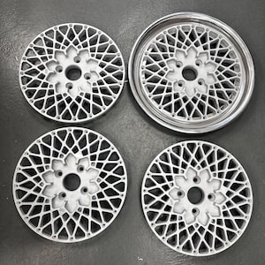 Puede incluir: Cuatro llantas de aleación de plata para automóviles con un diseño de radios geométricos complejos. Las ruedas tienen un buje central con múltiples orificios para pernos y un borde exterior pulido. El intrincado patrón crea una estética visualmente impactante y moderna.