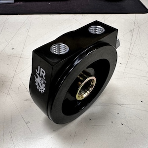 Puede incluir: Adaptador de filtro de aceite negro con dos puertos roscados y un logotipo de JR Racing.
