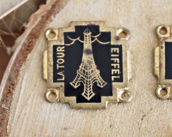 May include: Four gold-coloured metal charms with black enamel and gold accents. The charms feature images of the Eiffel Tower, the Arc de Triomphe, and two fleur-de-lis.