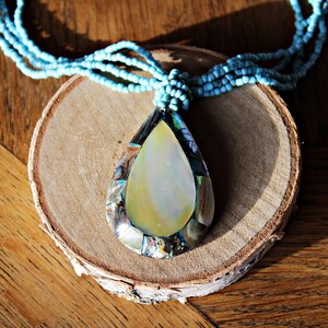 May include: A turquoise beaded necklace with a large iridescent abalone shell pendant. The pendant is shaped like a teardrop and has a natural, organic look.