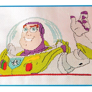 May include: Cross-stitch pattern of Buzz Lightyear from the Toy Story movie. The pattern features Buzz in his space ranger suit with a purple vest and a green and yellow spacesuit. He is smiling and has his arm raised in a wave.