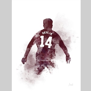 Op de afbeelding: Waterverfprint van een bordeauxrood shirt met de naam "Devlin" en het nummer "14" op de rug. Het kunstwerk toont een silhouet van een persoon in sportkleding, met een aquareleffect. De woorden "My Inspiration" zijn ook zichtbaar.