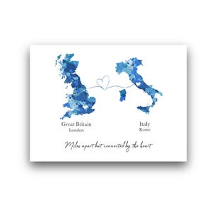 Puede incluir: Impresión blanca con mapas de acuarela azules de Gran Bretaña e Italia, conectados por un corazón. El texto incluye "Great Britain, London" e "Italy, Rome". También está presente la frase "Miles apart but connected by the heart".