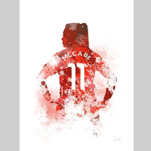 Könnte beinhalten: Aquarellmalerei eines Fußballspielers, der ein rotes Trikot mit dem Namen "MCCABE" und der Nummer "11" auf dem Rücken trägt.