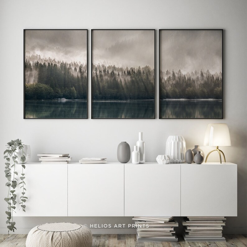 May include: A set of three framed prints depicting a misty forest scene with a lake in the foreground. The prints are in black frames and are hung on a white wall.