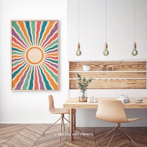 May include: A retro-style sunburst print with a colorful striped design in shades of orange, red, purple, blue, and green. The sunburst is centered around a white circle with a light brown background.