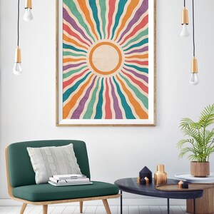 May include: A framed print of a colorful sunburst design with a white circle in the center. The sunburst is made up of wavy lines in shades of orange, red, purple, green, and blue. The print is hanging on a white wall in a living room setting.