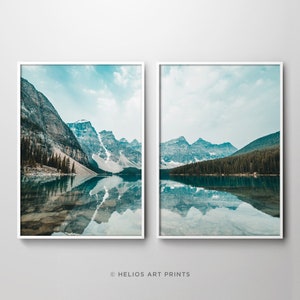 May include: Two framed landscape photographs of a mountain lake with a reflection of the mountains in the water. The lake is surrounded by trees and mountains. The sky is blue with some clouds.