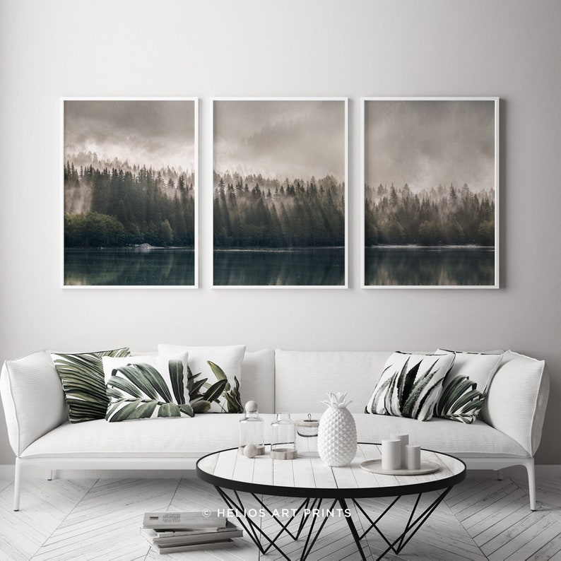 May include: A set of three framed prints depicting a misty forest scene with a lake in the foreground. The prints are in a modern style with a white frame and a muted colour palette.