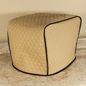 Puede incluir: Funda para electrodomésticos acolchada beige con ribete negro. La funda está diseñada para adaptarse a un electrodoméstico de encimera como un horno tostador o un procesador de alimentos.