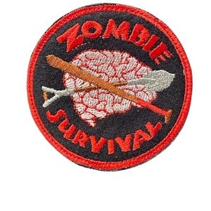 May include: A round, black and red embroidered patch with the text "Zombie Survival" and a white brain with a crossed shovel and baseball bat.