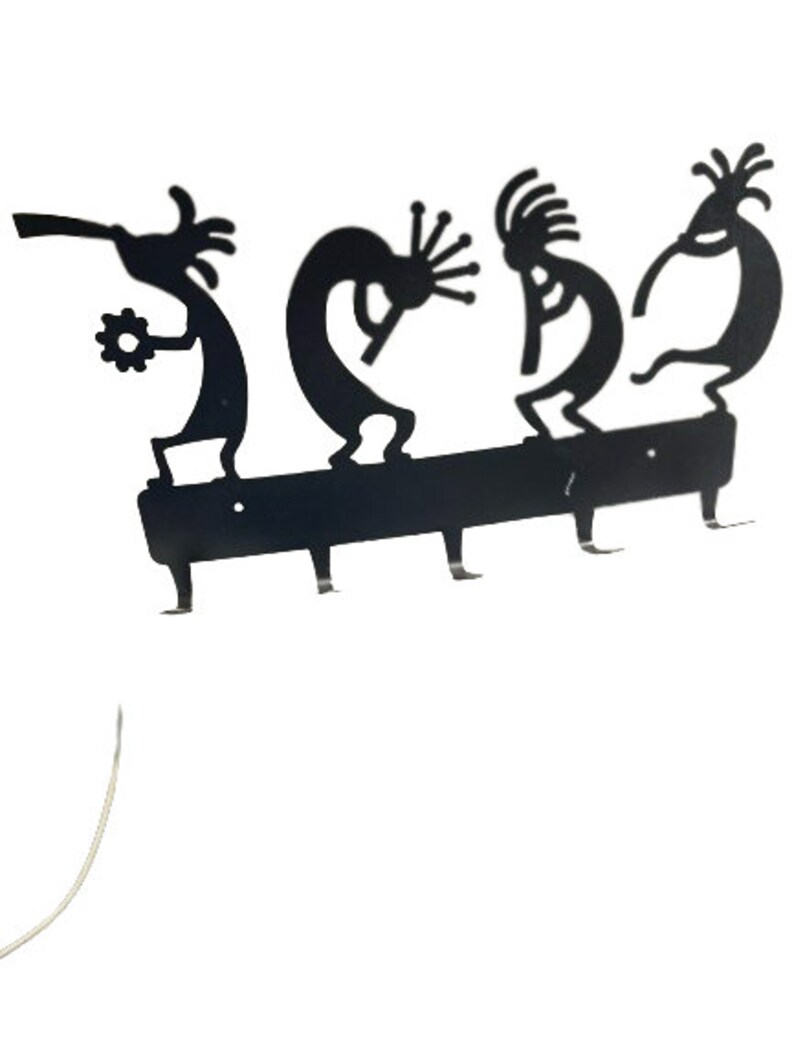 May include: Black metal key holder with four hooks shaped like stylized dancers. The key holder is mounted on a black metal bar.