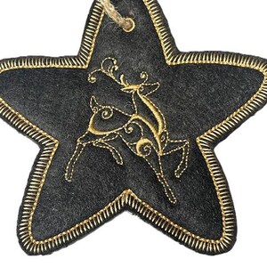 Op de afbeelding: Een zwarte viltster-versiering met een gouden geborduurd rendiermotief. De ster heeft een lus van touw aan de bovenkant om op te hangen.