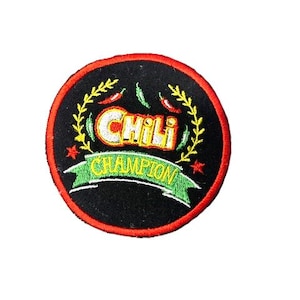 Può includere: Una toppa rotonda nera ricamata con un bordo rosso. La toppa presenta una ghirlanda verde con peperoncini rossi e il testo "Chili Champion" in giallo.