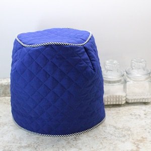 May include: A blue quilted cover for a kitchen appliance. The cover has a white and black trim around the top and bottom.