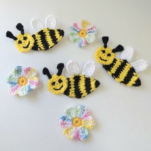 May include: Five crocheted bee and flower appliques. Three bees are yellow and black with white wings and smiling faces. Two flowers are multi-colored with yellow centers.