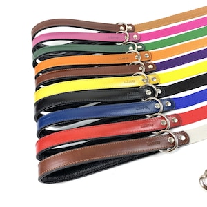 May include: A set of 12 leather dog leads in various colours, including black, brown, red, blue, yellow, orange, green, purple, pink, and tan. Each lead has a metal ring and the word "LINO" embossed on the leather.