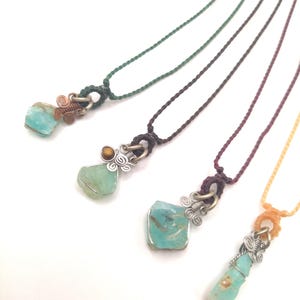 Può includere: Quattro collane con ciondoli in pietra turchese blu avvolti in filo d'argento. Ogni collana ha un cordoncino di colore diverso: verde, bordeaux, marrone e arancione.