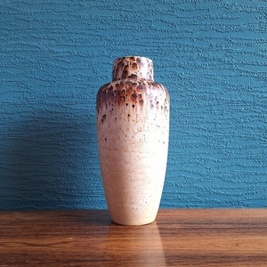 May include: A white ceramic vase with brown speckles and drips. The vase has a rounded bottom and a narrow opening.