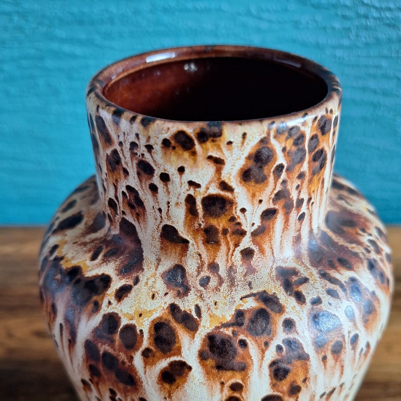 May include: A brown and white ceramic vase with a speckled pattern. The vase has a wide mouth and a rounded body.