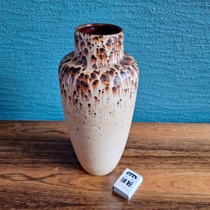 May include: A white ceramic vase with brown speckles and a drip glaze effect. The vase is tall and narrow with a rounded bottom and a slightly flared opening.