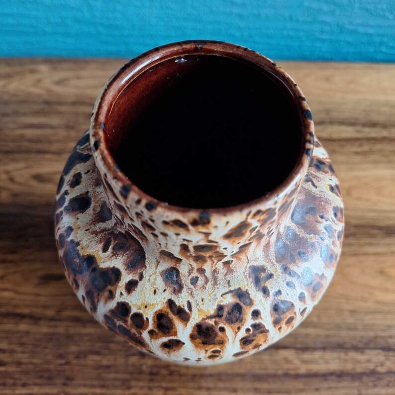 May include: A brown and white ceramic vase with a speckled pattern. The vase has a wide opening and a rounded body.