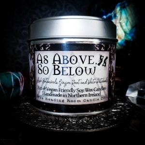 Pode incluir: Uma lata de vela prateada com um rótulo preto que diz "AS ABOVE, SO BELOW Lush Botanicals, Ginger Root and White Patchouli Eco & Vegan Friendly Soy Wax Candles Handmade in Northern Ireland The Reading Room Candle Co."