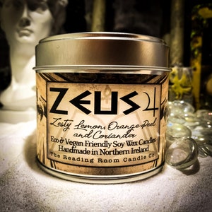 May include: A silver tin candle with a black and white label that reads "ZEUS" in a bold font. The label also says "Zesty Lemon, Orange Peel and Coriander" and "Eco & Vegan Friendly Soy Wax Candles Handmade in Northern Ireland The Reading Room Candle Co."