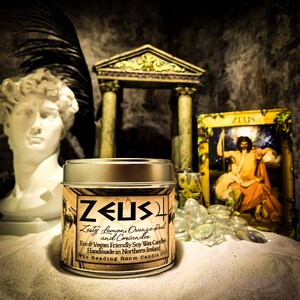 May include: A silver tin candle with a gold label that reads "ZEUS" in a stylized font. The label also says "Zesty Lemons, Orange Peel and Coriander" and "Eco & Vegan Friendly Soy Wax Candles Handmade in Northern Ireland The Reading Room Candle Co."