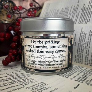 May include: A silver tin candle with a black and white label that reads "By the pricking of my thumbs, something wicked this way comes." The candle is labeled "Darkly Fragrant Fig and Spiced Orange Eco & Vegan Friendly Soy Wax Candles Handmade in Northern Ireland The Reading Room Candle Co."