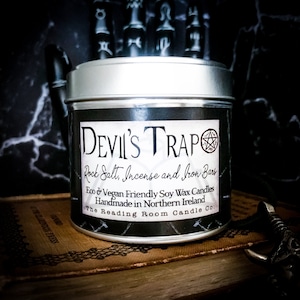 May include: A silver tin candle with a black label that reads "DEVIL'S TRAP Rock Salt, Incense and Iron Bars Eco & Vegan Friendly Soy Wax Candles Handmade in Northern Ireland The Reading Room Candle Co."