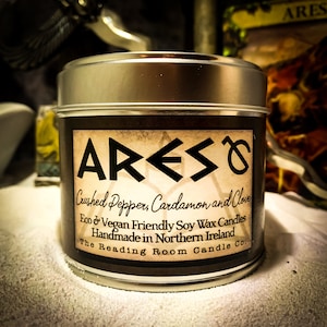 Puede incluir: Una vela en una lata de plata con una etiqueta marr&oacute;n que dice "ARES Crushed Pepper, Cardamon and Clove Eco & Vegan Friendly Soy Wax Candles Handmade in Northern Ireland The Reading Room Candle Co."