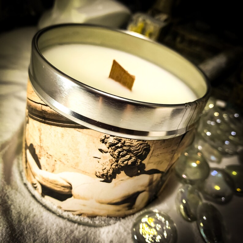 May include: A silver candle tin with a white candle and a wooden wick. The tin has a vintage image of a man with a beard on it.
