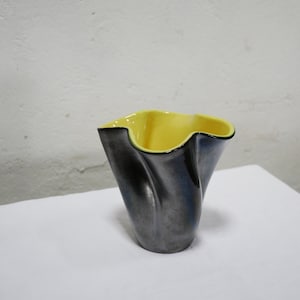 May include: A black ceramic vase with a yellow interior. The vase has a unique, wavy design.