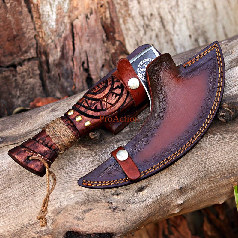 May include: A handcrafted knife with a wooden handle and a leather sheath. The handle is intricately carved with a geometric design and wrapped with twine. The sheath is brown leather with decorative stitching and a snap closure. The knife is resting on a wooden surface.