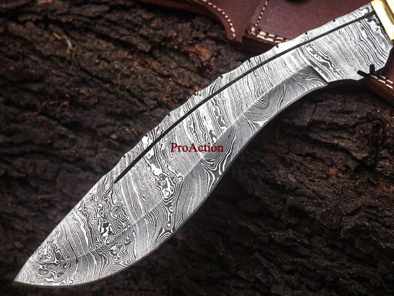 May include: Close-up of a Damascus steel knife blade with a curved edge. The blade has a unique, swirling pattern in shades of silver and black. The text "ProAction" is visible on the blade. The knife is likely for hunting or outdoor use.