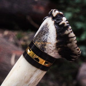 Puede incluir: Primer plano de un mango de cuchillo. El mango est&aacute; hecho de material color hueso con una banda negra y dorada. La parte superior del mango tiene un patr&oacute;n texturizado marr&oacute;n oscuro y blanco. El mango del cuchillo est&aacute; sobre un fondo borroso.