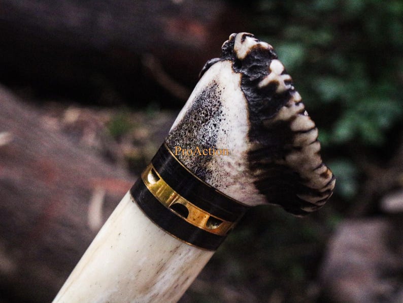Puede incluir: Primer plano de un mango de cuchillo. El mango est&aacute; hecho de material color hueso con una banda negra y dorada. La parte superior del mango tiene un patr&oacute;n texturizado marr&oacute;n oscuro y blanco. El mango del cuchillo est&aacute; sobre un fondo borroso.
