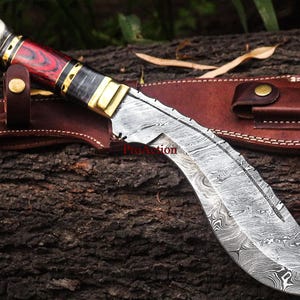 May include: A Damascus steel kukri knife with a red and black wooden handle, brass accents, and a leather sheath. The blade has a distinctive curved shape and a patterned surface. The knife is designed for outdoor use.
