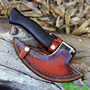May include: A handcrafted knife with a dark wooden handle and a brown leather sheath. The sheath features decorative stitching and a button closure. The knife is partially sheathed, revealing a portion of the blade.