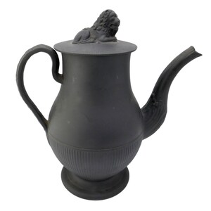 May include: Black ceramic teapot with a lion finial on the lid. The teapot has a rounded body with a fluted design and a spout on the side.