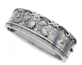 Puede incluir: Un brazalete de plata con un diseño floral grabado. El brazalete es de forma ovalada y tiene un cierre con bisagra.