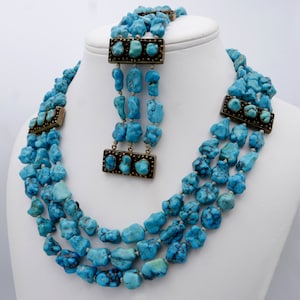 May include: A turquoise and silver multi-strand necklace and bracelet set. The necklace is made of turquoise stones and silver beads. The bracelet is made of turquoise stones and silver beads. The set is on a white background.