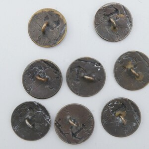 May include: Eight antique brass buttons with a raised design and a loop on the back. The buttons are circular and have a worn, aged appearance.
