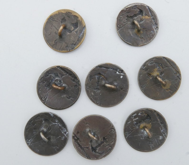 May include: Eight antique brass buttons with a raised design and a loop on the back. The buttons are circular and have a worn, aged appearance.